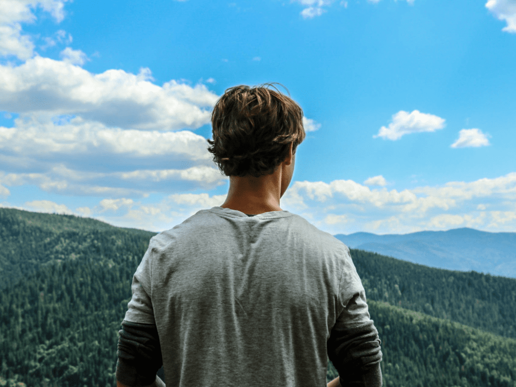 back of man looking out over mountains with blue sky